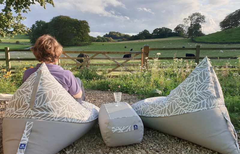Two outdoor patio bean bags in a gravel seating area. Between the bean bags is a low table/footstool with a glass on it.