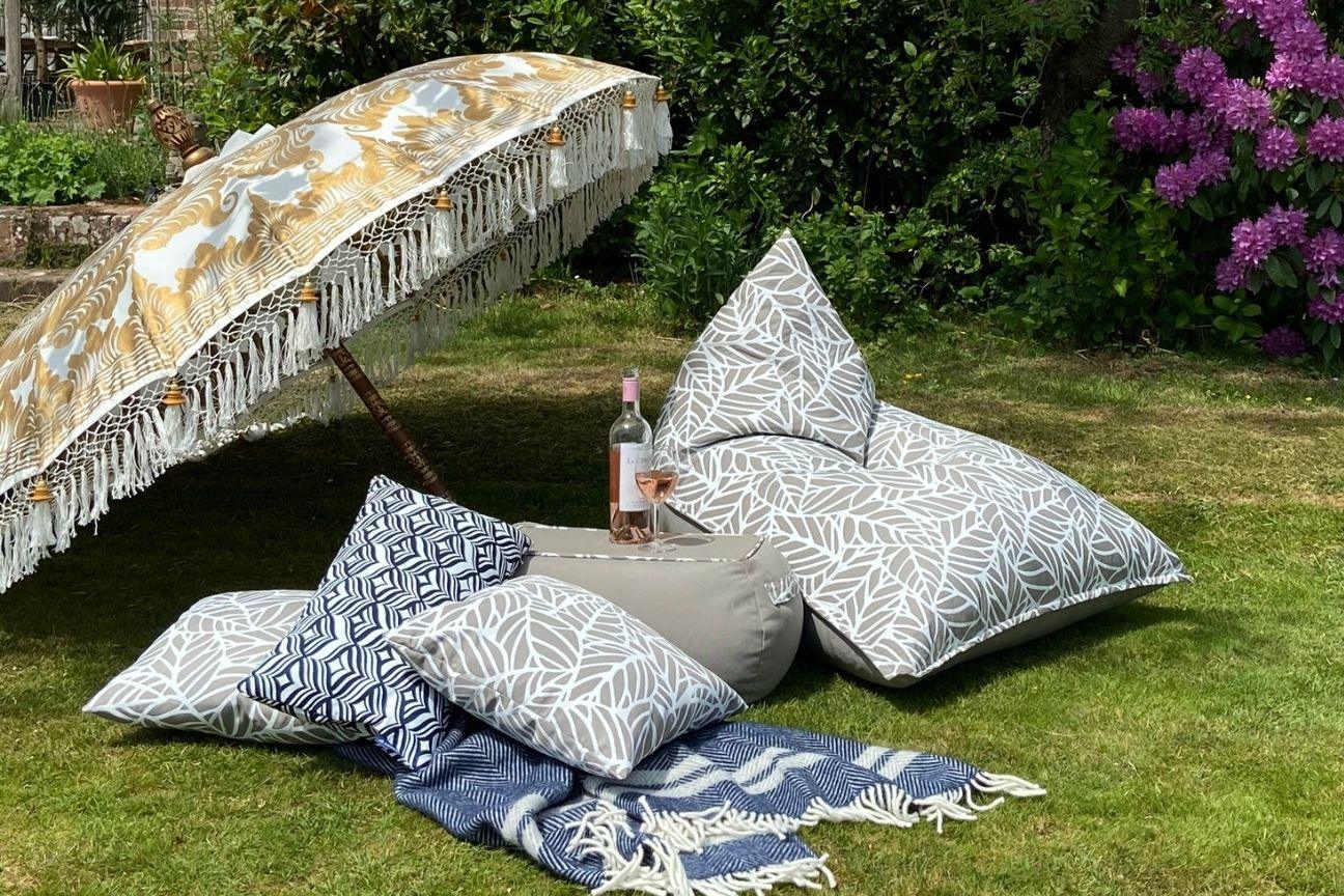 Outdoor bean bag chair and table on grass under a parasol.