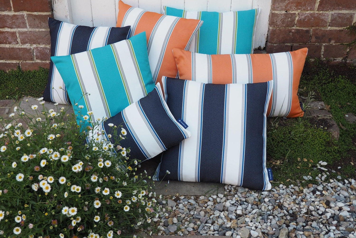 Outdoor cushions in a pile on a garden patio. They are striped in navy and white, turquoise and wite, and orange and white.