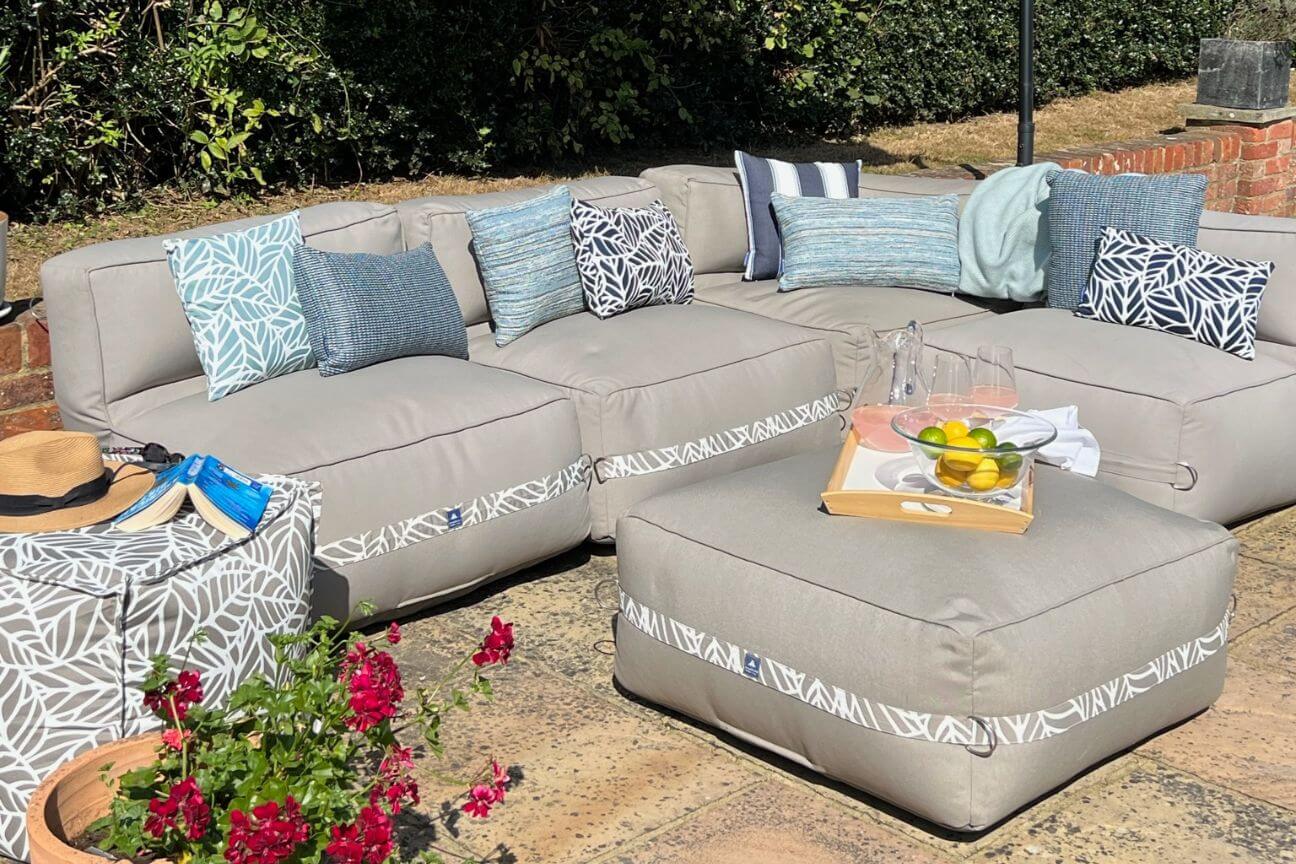 Comfortable fabric garden sofa covered with luxury blue and white texxtured throw cushions on a sunny patio.