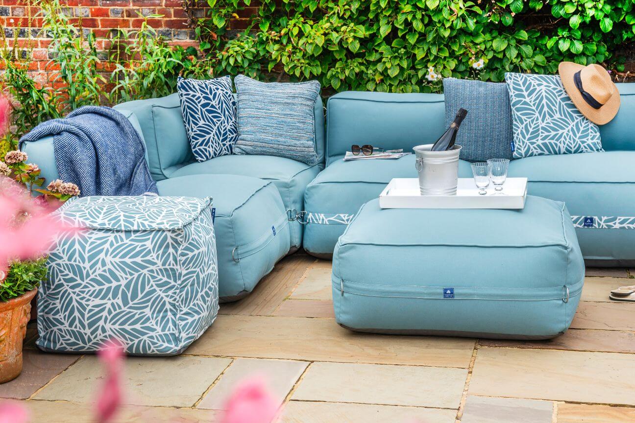 Blue comfortable garden sofa covered with cushions and laid out ready for a garden party.