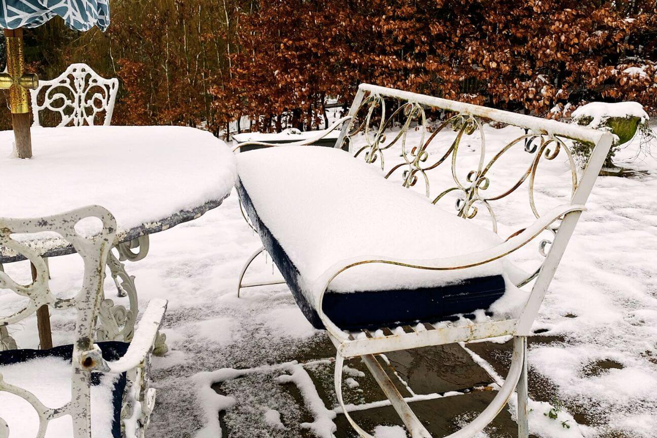 White metal bench with a navy blue seat cushion covered with a thick layer of snow.