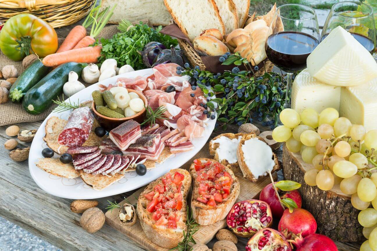 Wooden table overflowing with fruit, cheese, charcuterie, and ciabatta.