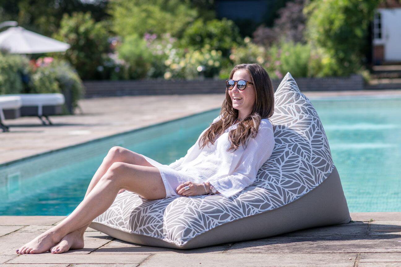 A woman relaxes and smiles on a bean bag in the sunshine.