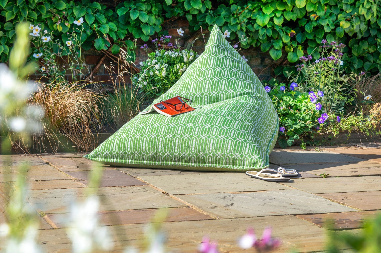 Outdoor bean bag chair in Green calypso on a patio with flowers and plants in the background
