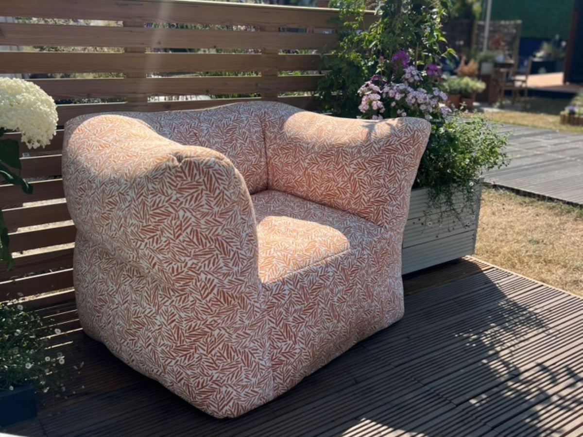 A modern low-profile outdoor bean bag armchair with a dense orange and white abstract leaf-like patterned fabric, set outdoors on a decking.
