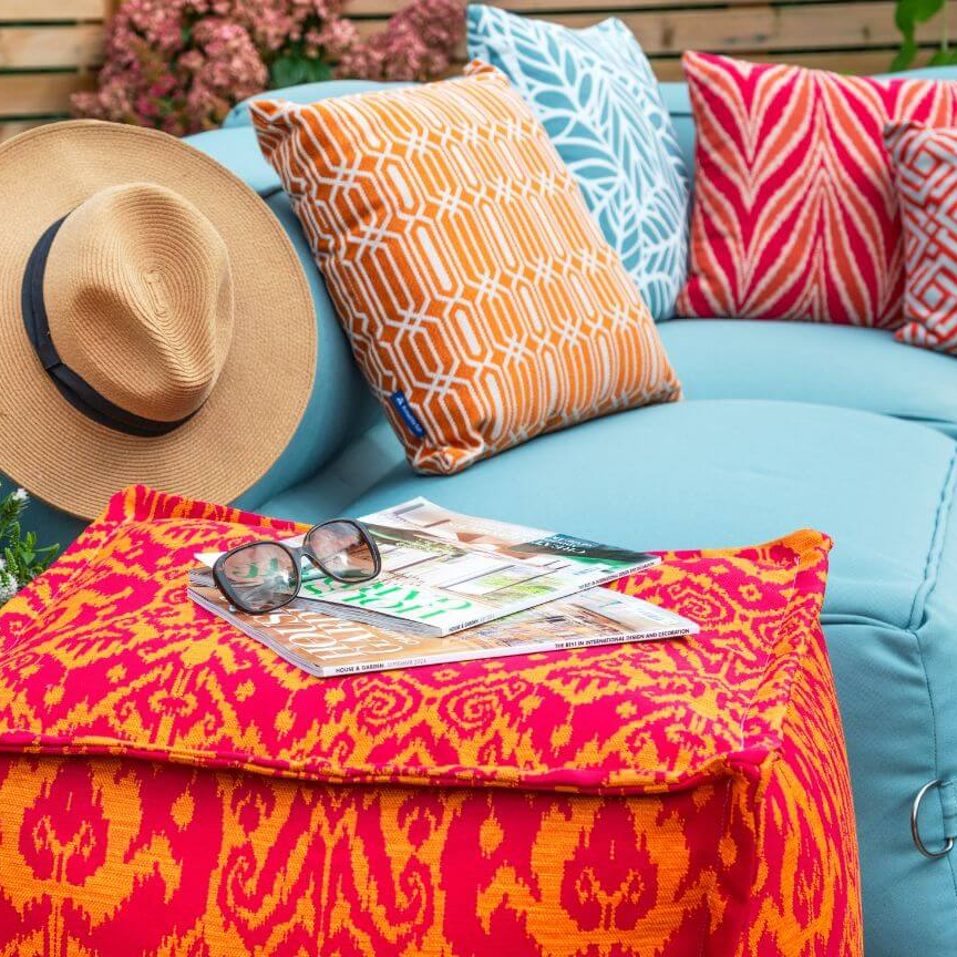 Colorful outdoor setting with a blue sofa, patterned cushions, and a straw hat.