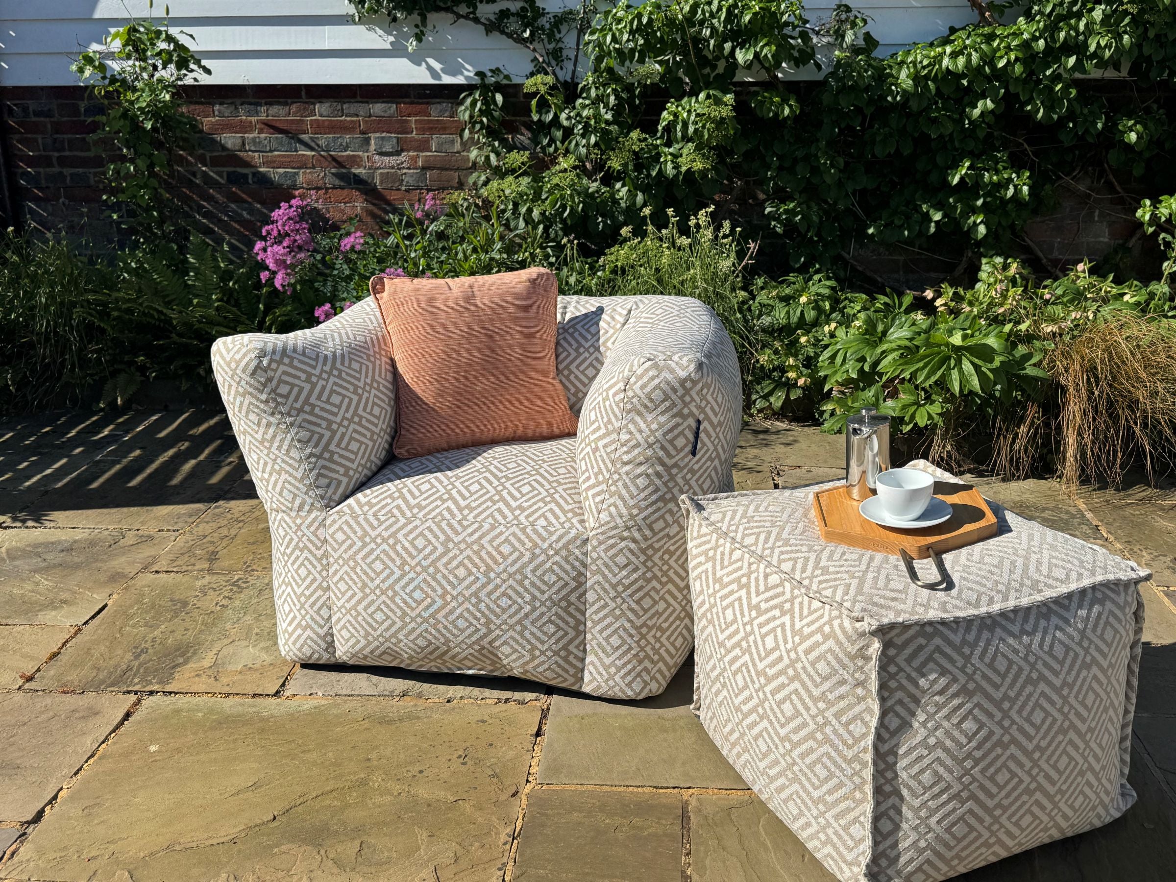 garden bean bag armchair in natural sigma with matching pouffe. decorated with pinstripe orange outdoor cushion. 100% british-made, stain-proof, water-resistant with 5 year guarantee