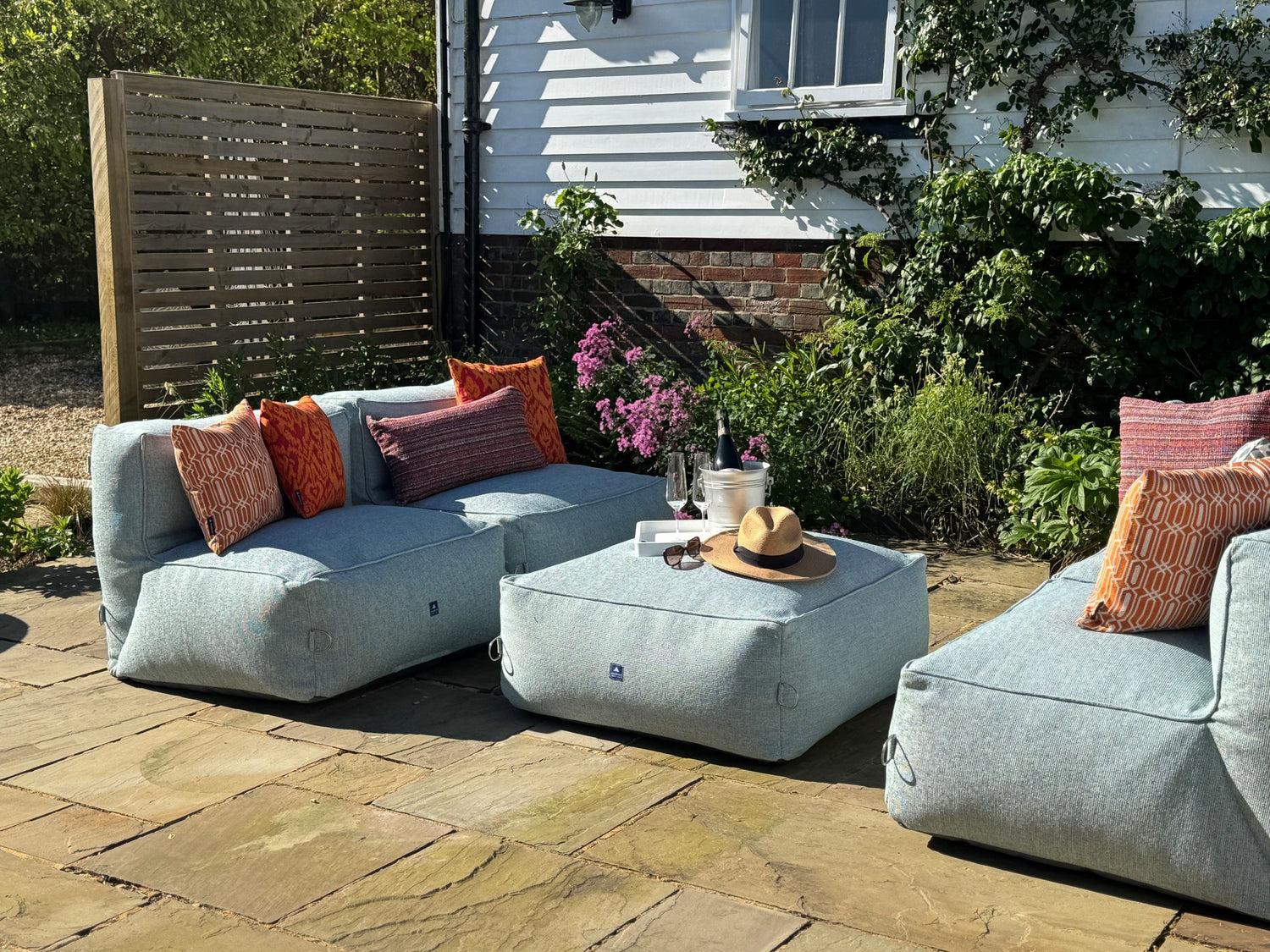 garden bean bag dining sofa set consisting of 4 chairs and 1 ottoman in ocean spray. decorated with orange cushions in calypso, woven tropic and medina tropic. 100% British made, water-resistant, stain-proof with 5 year guarantee