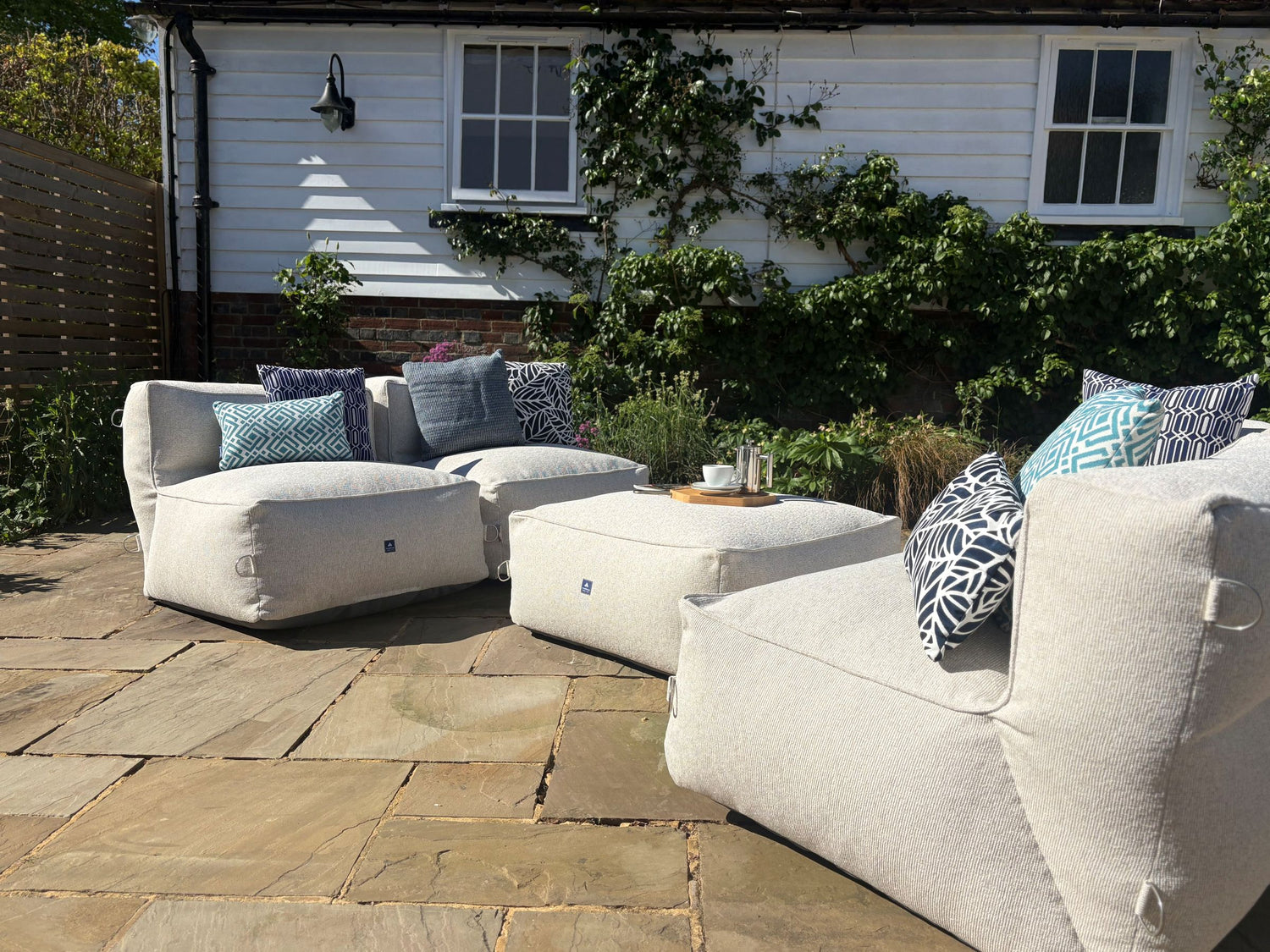 garden bean bag dining sofa set in natural shell consisting of 4 chairs and 1 ottoman. decorated with blue cushions in sigma, calypso, woven and palm patterns. 100% british made, water-resistant, stain-proof with 5 year guarantee