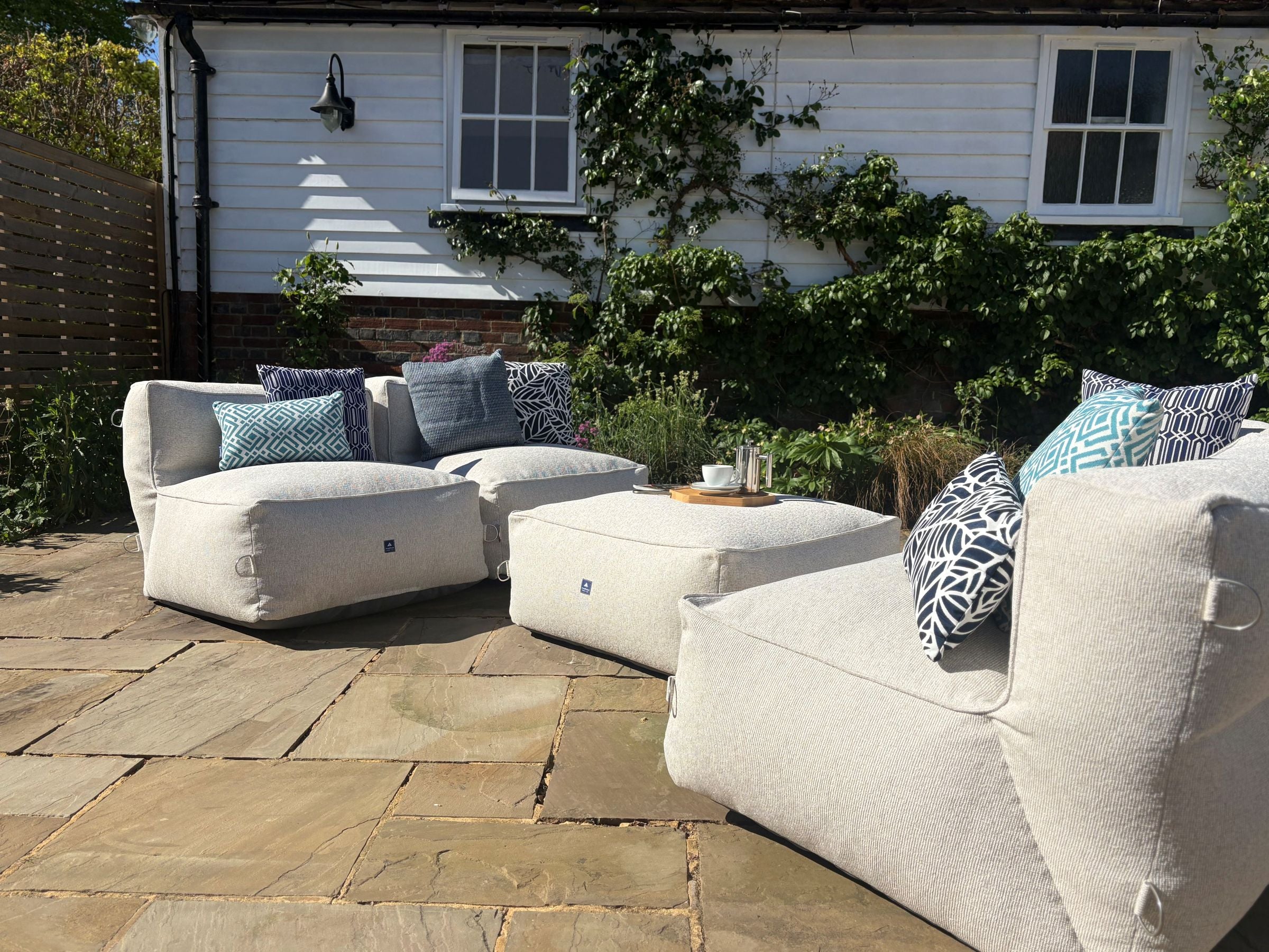 garden bean bag dining sofa set in natural shell consisting of 4 chairs and 1 ottoman. decorated with blue cushions in sigma, calypso, woven and palm patterns. 100% british made, water-resistant, stain-proof with 5 year guarantee