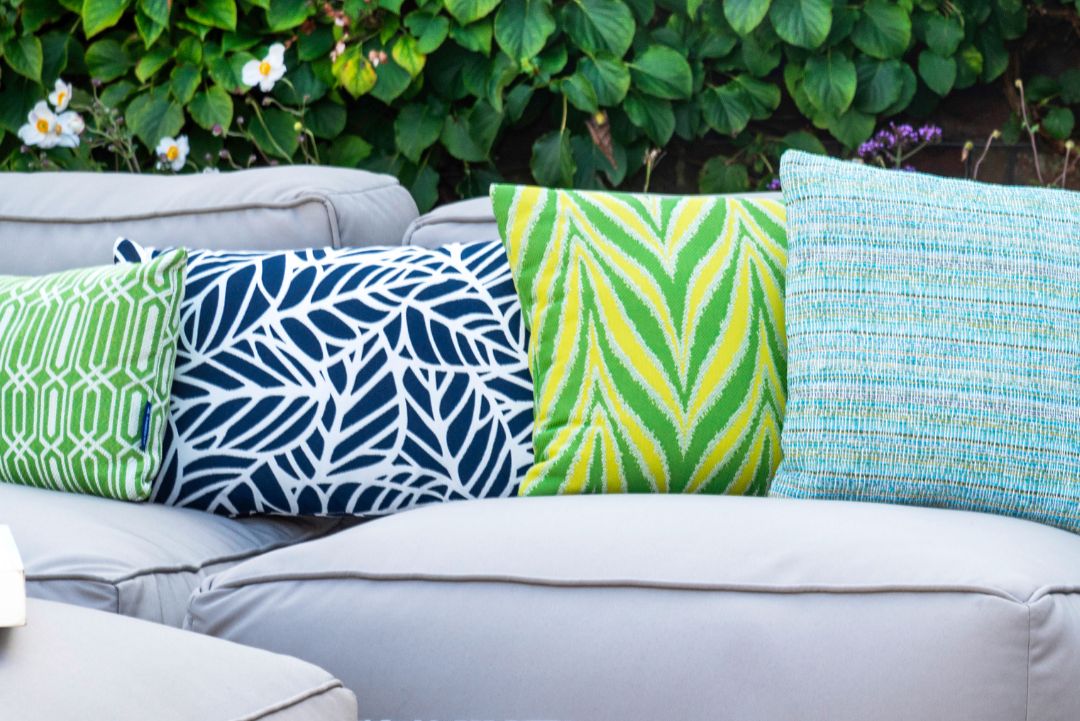 A green and yellow flame-patterned cushion on a garden sofa with other green and blue outdoor cushions.