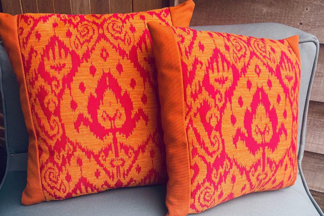 Two square garden cushions made from orange and pink waterproof fabric, patterned on the front and pinstripe on the sides.