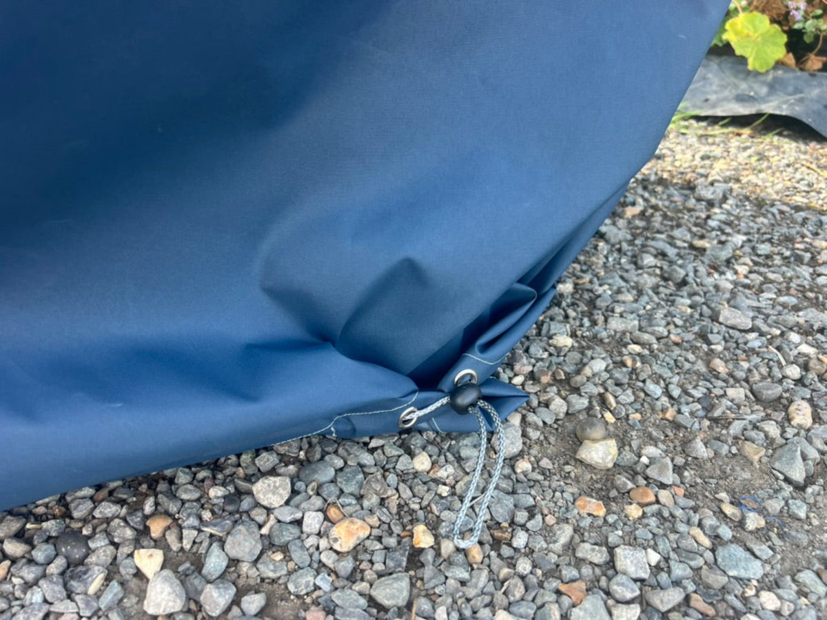 Close-up of a waterproof cover for modular corner chair or armchair for winter use. Secured with metal grommets and a drawstring cord, resting on gravel outdoors.