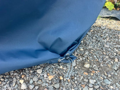 Close-up of a waterproof cover for modular corner chair or armchair for winter use. Secured with metal grommets and a drawstring cord, resting on gravel outdoors.