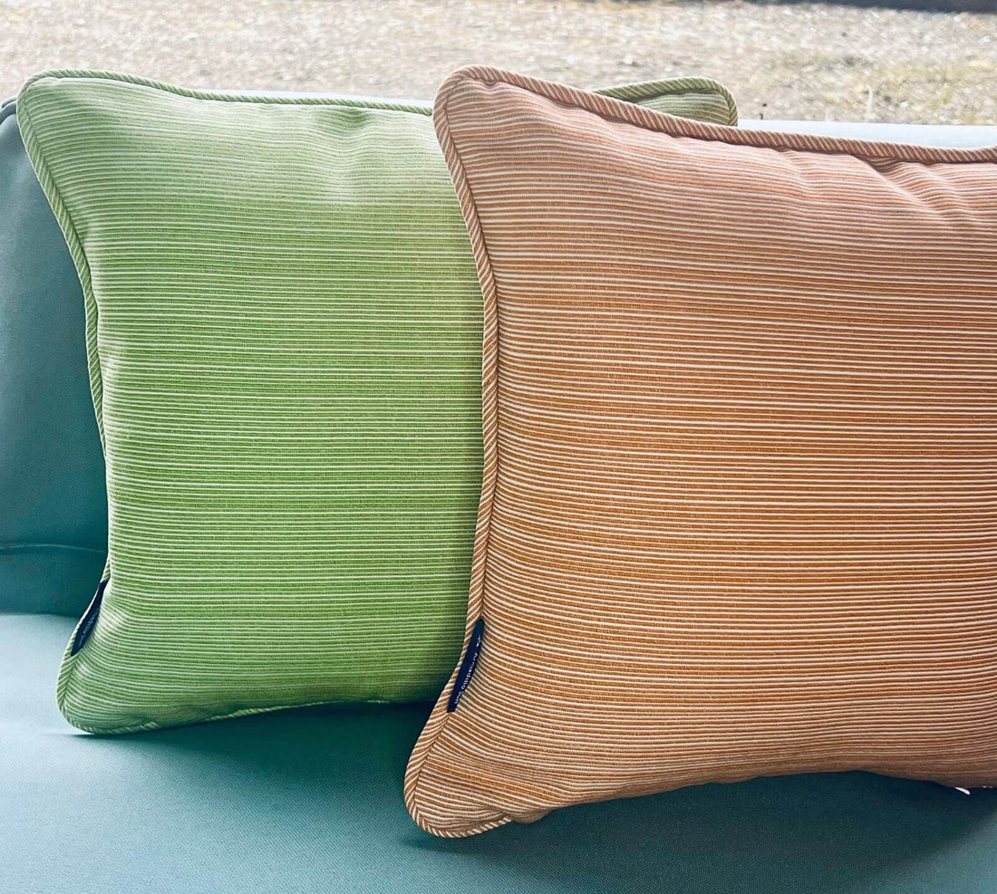 Two woven outdoor cushions withe subtle ribbing, One is in shades of green and the other in orange and white.