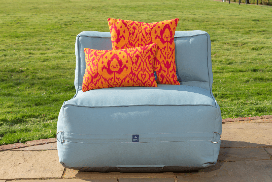 Two garden throw cushions in a dynamic orange and pink fabric on a outdoor sofa chair.